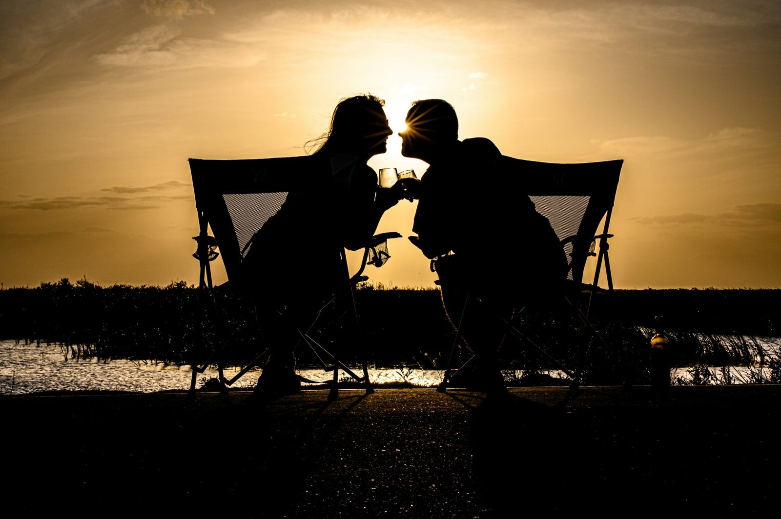 a couple of people sitting on a bench with a sunset in the background